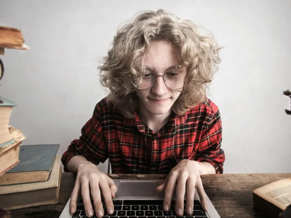 Ein Mädchen sitzt umgeben von Büchern an einem Laptop und schreibt.